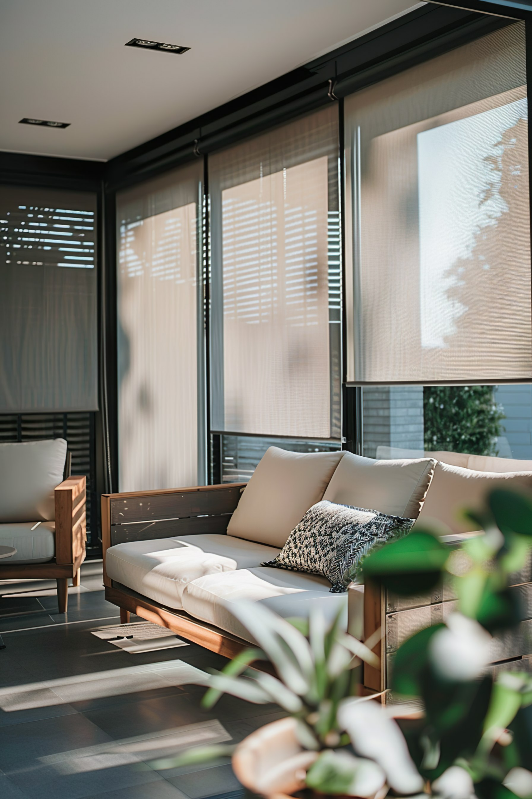 Modern sunlit living room with sheer window blinds, comfortable seating, and a green plant in the foreground.