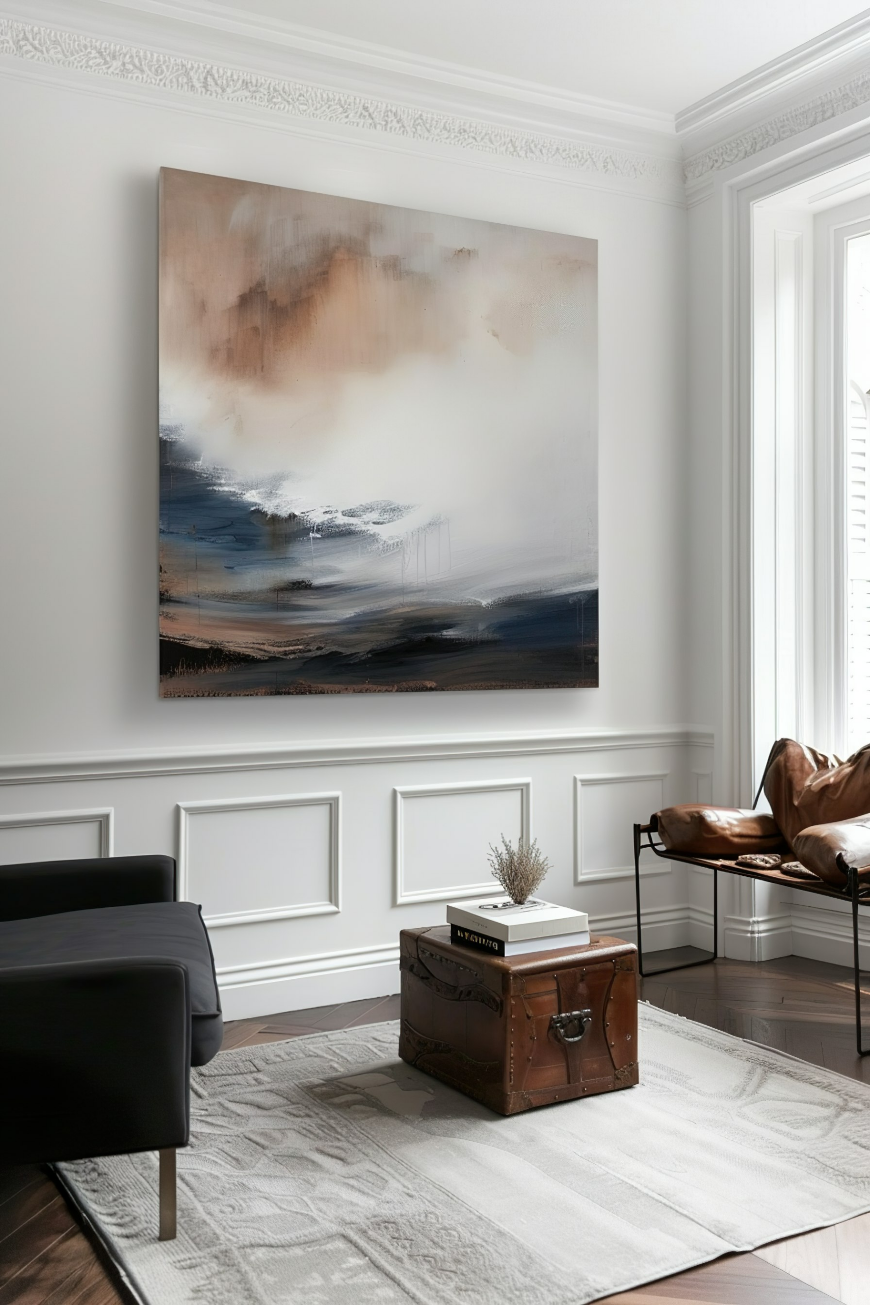 Abstract painting on a white wall above a black sofa, with a brown leather chair and vintage trunk in an elegant room.