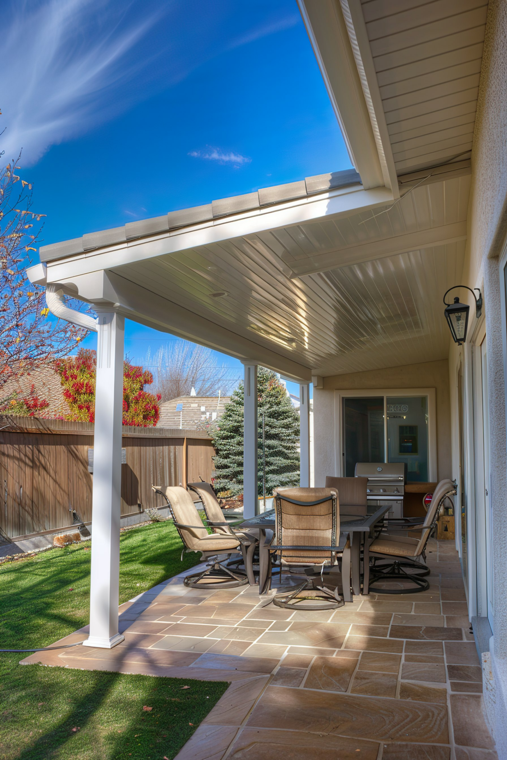 ALT: A cozy patio area with a dining set and lounging chairs under a pergola, with a clear blue sky above and a manicured lawn in the background.