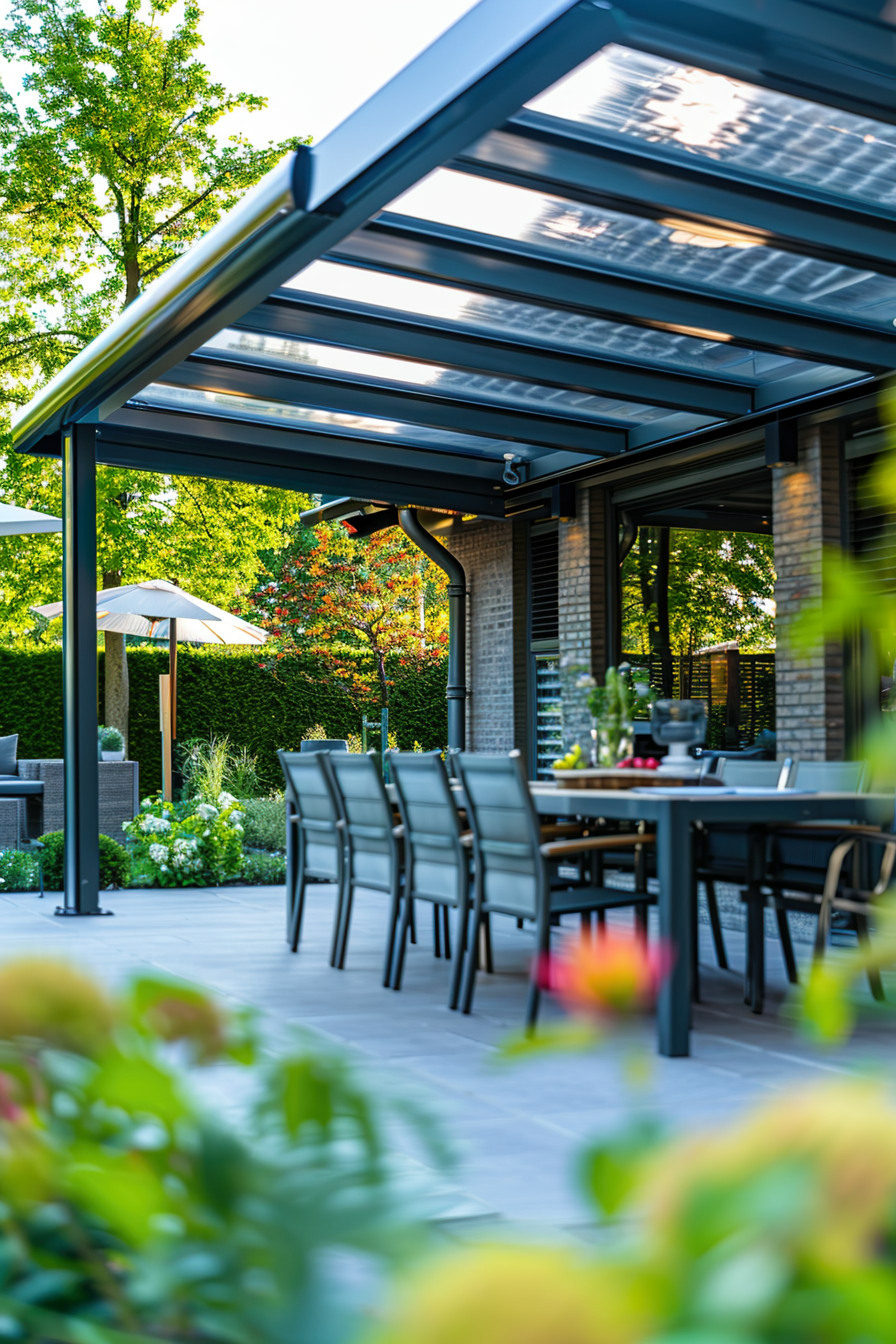 ALT: A modern outdoor patio with a dining table and chairs under a pergola, surrounded by lush garden foliage in a residential backyard.