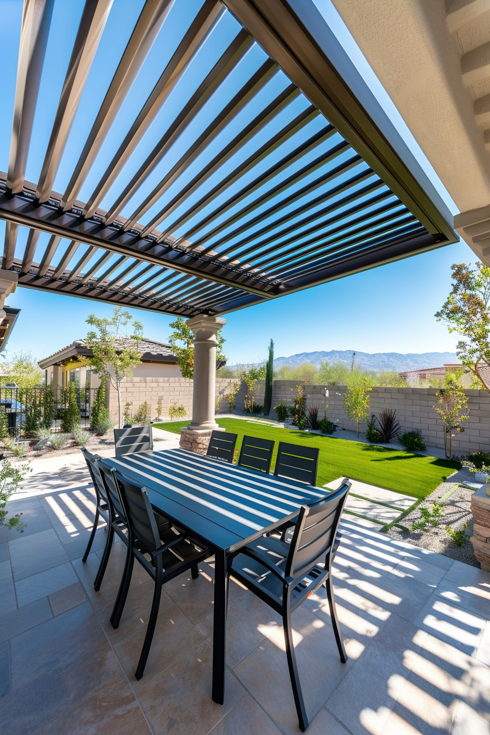 Outdoor patio with modern furniture under a pergola, overlooking a garden with a clear blue sky above.