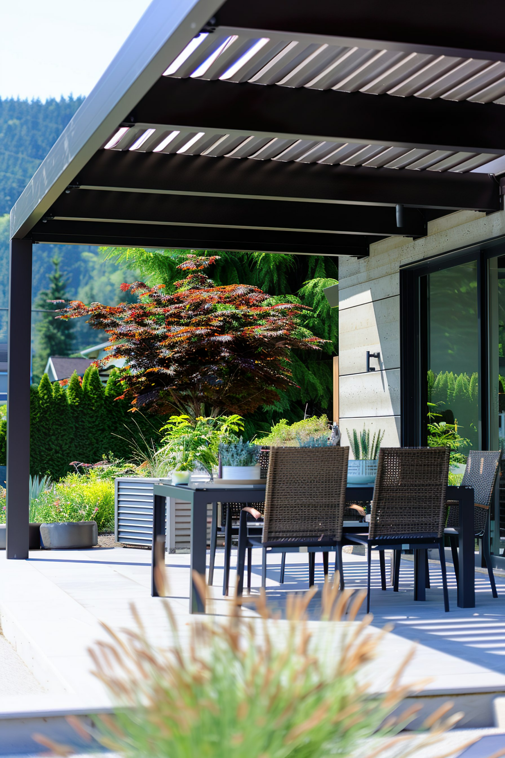 Outdoor patio with modern furniture under a pergola, overlooking a lush garden with a mountain in the distance.