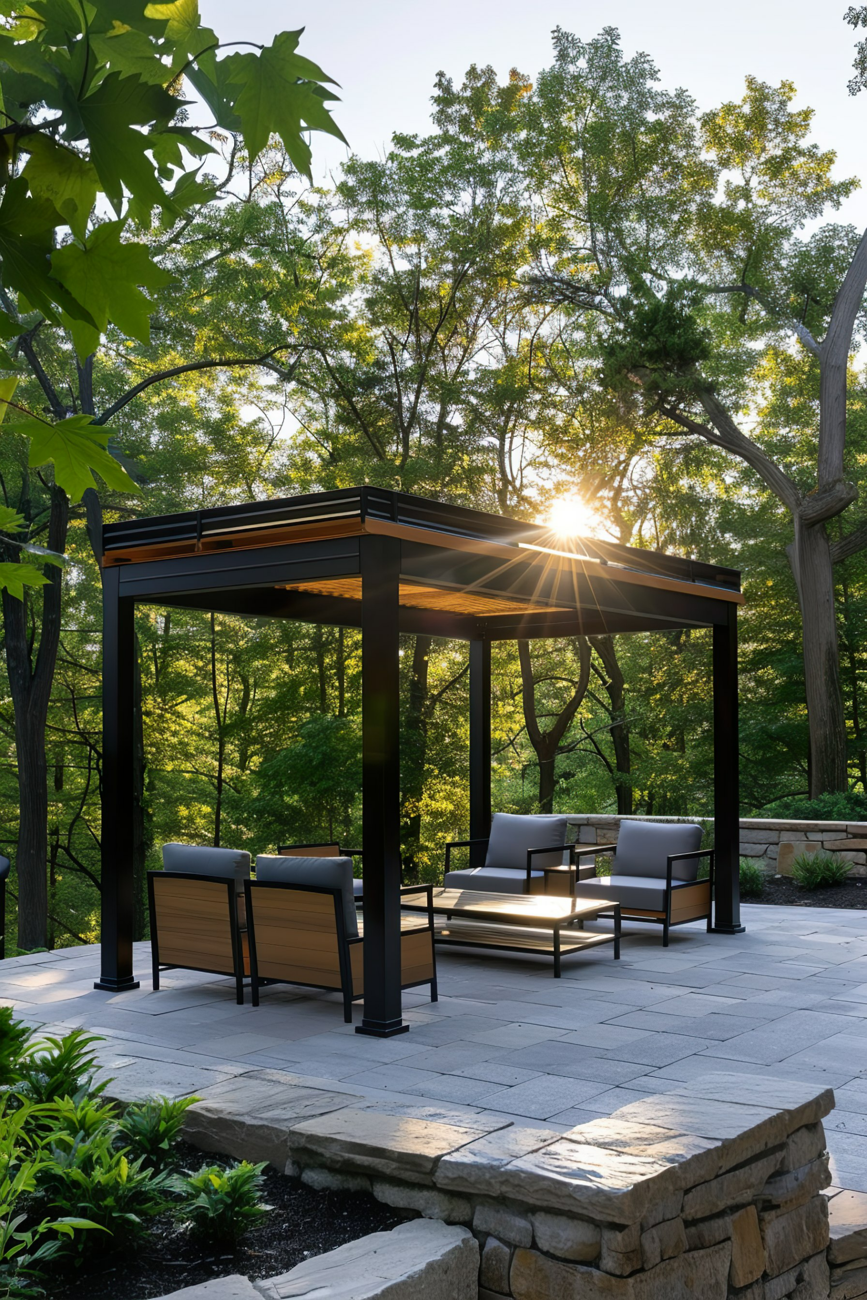 Modern outdoor pergola with lounging chairs on a stone patio surrounded by lush trees at sunset.